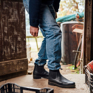 Person wearing Blundstone Boots 600 Series and blue jeans standing in a rustic outdoor setting with crates and wooden furniture.