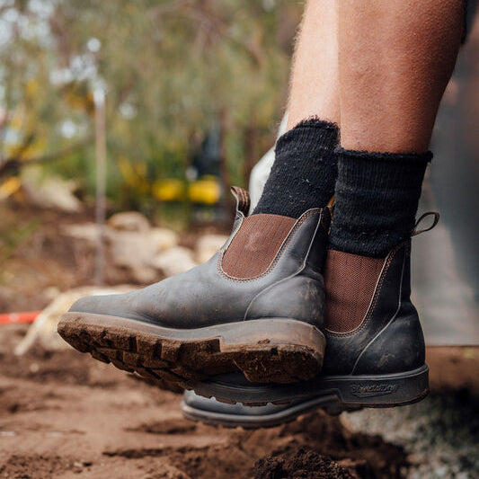 Person wearing Blundstone Boots 600 Series with brown soles on a muddy ground.